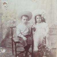Et meget gammelt billede af to børn med, en dreng siddende på en stol, en pige med en blomsterkurv