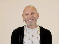 en mand der smiler med piercinger og tatoveringer i ansigtet